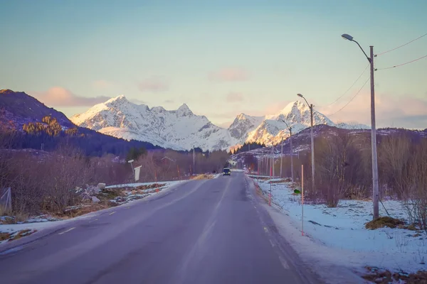 Rua congelada com um carro na estrada em Skjelfjord, com uma enorme montanha coberta de neve nas ilhas Lofoten — Fotografia de Stock