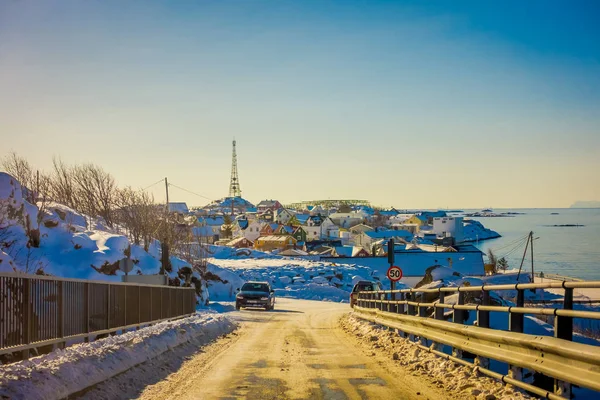 Henningsvaer, Noruega - 10 de abril de 2018: Vista ao ar livre da rua congelada coberta de neve e carros na estrada com alguns edifícios na horizontal durante um dia ensolarado — Fotografia de Stock