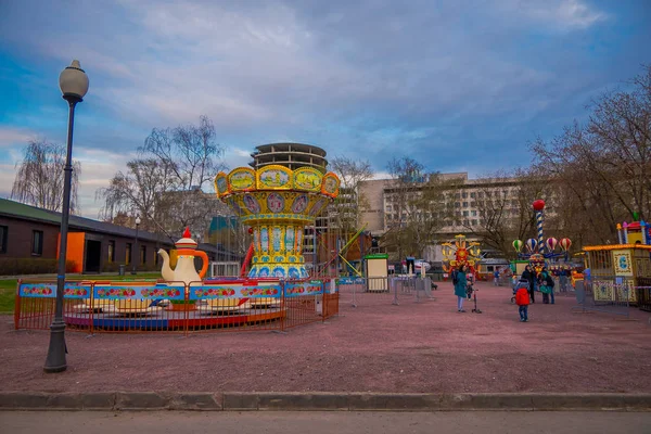 MOSCÚ, RUSIA - 24 DE ABRIL DE 2018: Vista al aire libre de las personas con sus hijos en un carrusel disfrutando del tiempo libre con diferentes juegos y caminando cerca del parque Gorky —  Fotos de Stock