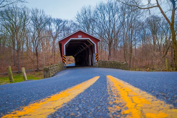 Primo piano della strada con linea gialla all'aperto con un ponte rosso coperto situato all'interno della foresta in una giornata nuvolosa a Lancaster — Foto Stock