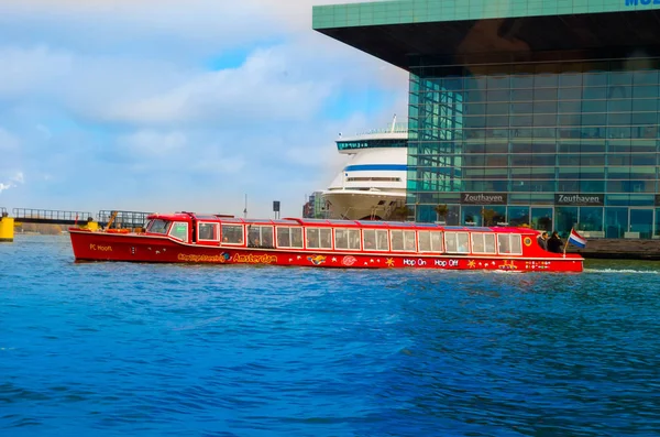 AMSTERDÃO, PAÍSES BAIXOS, 23 de abril de 2018: Vista ao ar livre do barco vermelho em uma costa do canal é a capital e cidade mais populosa da Holanda, com uma infra-estrutura de construção por trás — Fotografia de Stock