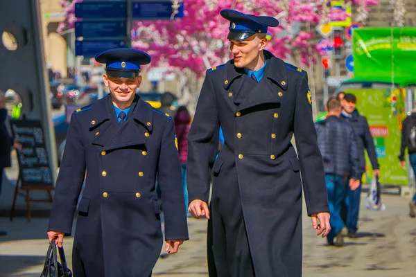 MOSCOW, RÚSSIA- ABRIL, 24, 2018: Vista ao ar livre de dois homens vestindo uniforme e andando sob luzes festivas de Natal nas ruas Nikolskaya em um dia ensolarado — Fotografia de Stock