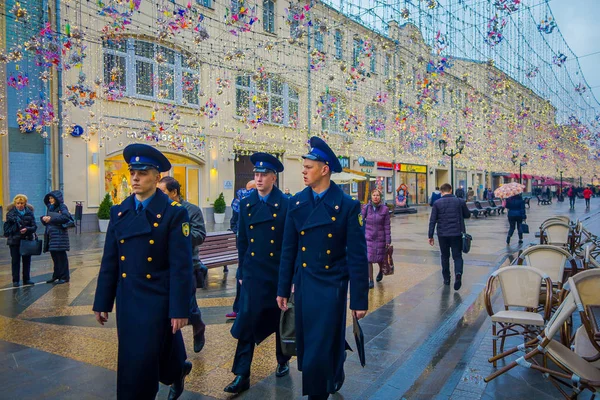 Moskva, Ryssland - April, 24, 2018: utomhus utsikt över grupp män bär blå marinblå uniform och gå nära en vanliga människor under en festlig julbelysning på Nikolskaya gatorna i en molnig dag — Stockfoto