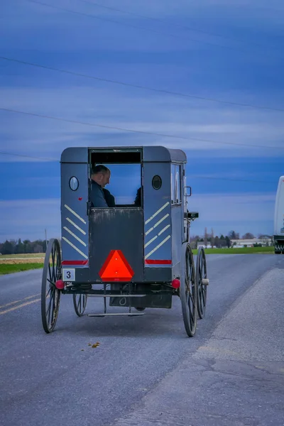 Pennsylvania, Usa, April, 18, 2018: Buiten uitzicht op de achterkant van een oude ouderwetse, Amish buggy met mensen binnen en een paardrijden op grind landelijke weg — Stockfoto