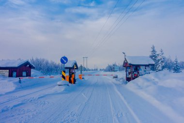 Bagnsasen, Norveç - Nisan, 02, 2018: kısmi bir yol ile Begnsasen bölgesine girmek için segurity denetim görünümünü şiddetli kar yağışı ve çam ağaçları içinde ahşap kulübe ormanıyla kaplı