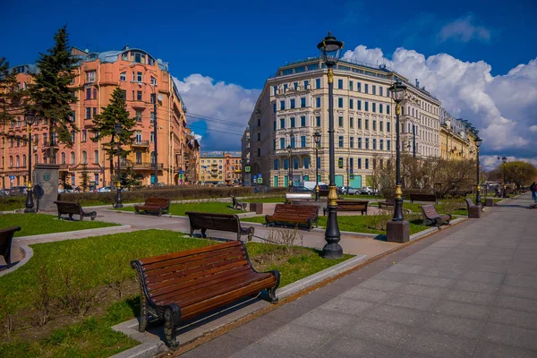 ST. PETERSBURG, RUSSIA, 01 MAY 2018: View od wooden public chairs in a park with huge buildings behind located in dowtown in St. Petersburg — Stock Photo, Image