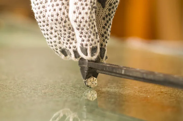 Main étroite portant des gants de travail blancs à l'aide d'un outil de coupe en métal sur un morceau de verre transparent — Photo