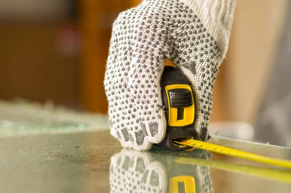 Main étroite portant des gants de travail blancs à l'aide d'un outil de mesure sur un morceau de verre transparent — Photo