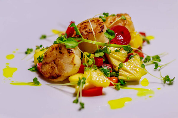 White ceramic plate with grilled King scallop with pineapple, onion colored with beetroot juice, red bell pepper, decorated with bean sprouts. Side view