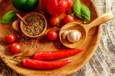 Taze kiraz domates, sarımsak, biber, fesleğen yaprakları, kırmızı ve yeşil capsicums, Kuru baharat ve ahşap masa üzerinde ahşap tepsi üzerinde tahta kaşıkla ahşap bir tencerede tuz karışımı. Üstten Görünüm.