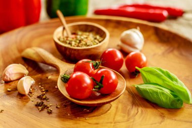 Taze kiraz domates, sarımsak, fesleğen yaprağı, ahşap masa üzerinde ahşap tepsi üzerinde tahta kaşıkla ahşap tencerede kuru baharat karışımı, kırmızı ve yeşil capsicums ve arka plan üzerinde pul biber. Yan görünüm. 