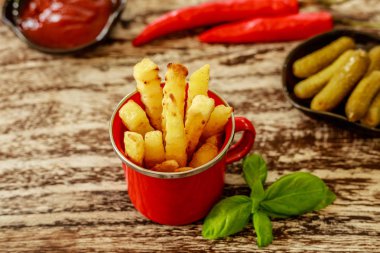 Kırmızı emaye fincan Patates kızartması ile servis domates sosu ve siyah seramik tencere salatalık turşusu ile dekore edilmiş fesleğen yaprakları ve kırmızı biber soğuk, ahşap masa üzerinde. Üstten Görünüm.