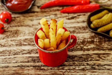 Kırmızı emaye fincan Patates kızartması ile servis domates sosu ve siyah seramik tencere salatalık turşusu ile dekore edilmiş olan kiraz domates ve kırmızı biber soğuk, ahşap masa üzerinde. Üstten Görünüm.