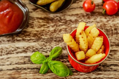 Kırmızı emaye fincan Patates kızartması ile servis domates sosu ve siyah seramik tencere salatalık turşusu ile dekore edilmiş fesleğen yaprakları ve kiraz domates, ahşap masa üzerinde. Üstten Görünüm.