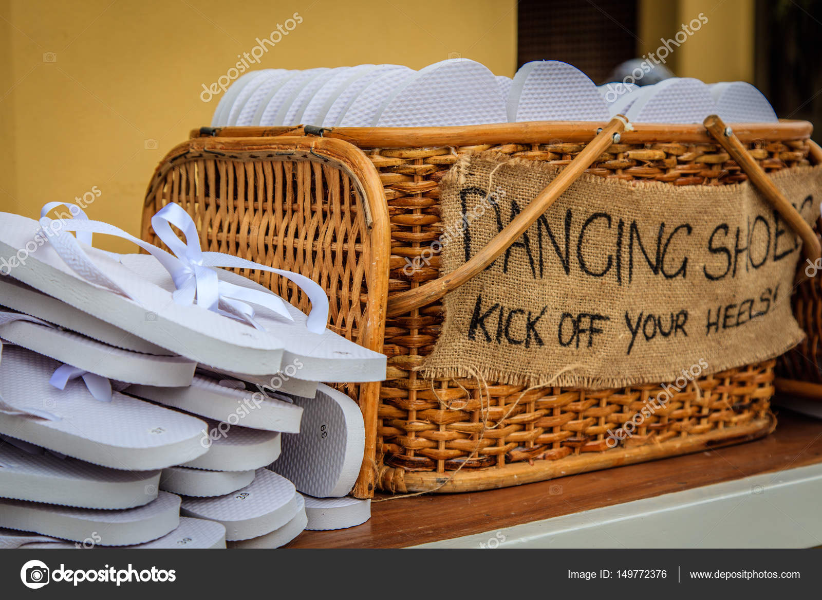 Rattan basket with white flip flops of different sizes for guests with a writing DANCING SHOES. KICK OFF YOUR HEELS Stock Photo GekkoGallary 149772376