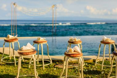 Wedding ceremony setup near the ocean at sunset - chairs for guests with flower petals and bamboo fans and a wedding arch clipart