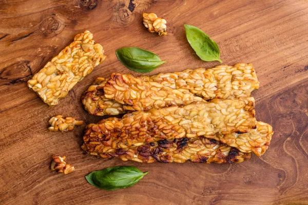 Fried Tempe ahşap yüzeyde fesleğen yaprakları ile dekore edilmiştir. Üstten Görünüm