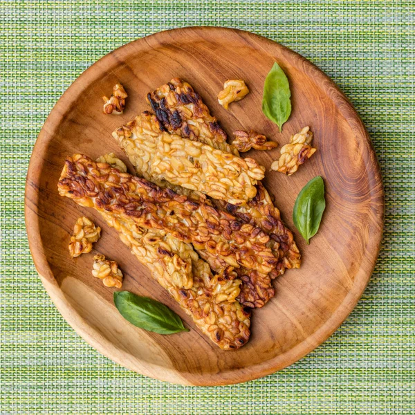 Fried Tempe yeşil peçete fesleğen yaprakları bir yuvarlak ahşap tepsi ile dekore edilmiştir. Üstten Görünüm. Kare görüntü.
