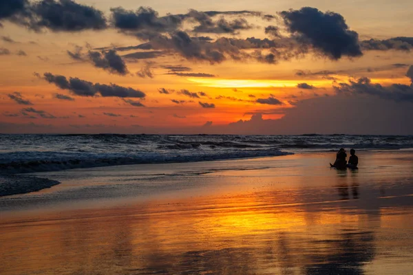 Gün batımında Berawa beach (Pantai Berawa). Siluetleri gelgit içinde oturan iki kişinin. Canggu, Bali, Endonezya.