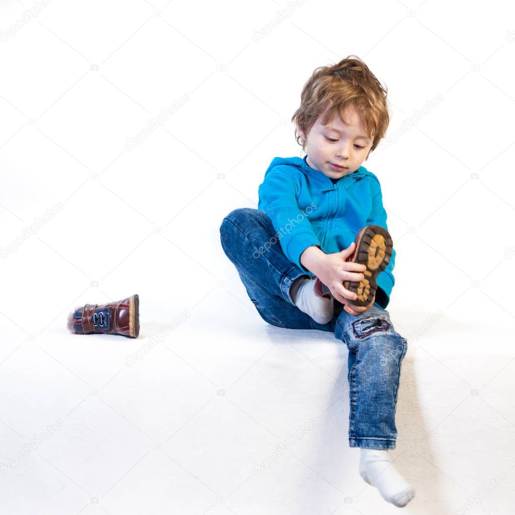 A little child of three years tries to wear shoes. Isolated on a