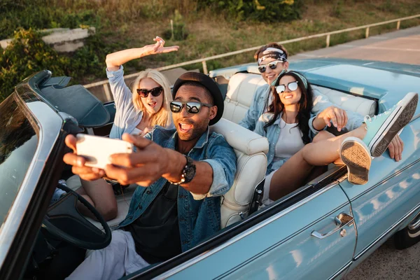 Joyful jóvenes amigos tomando selfie con teléfono móvil en cabriolet —  Fotos de Stock