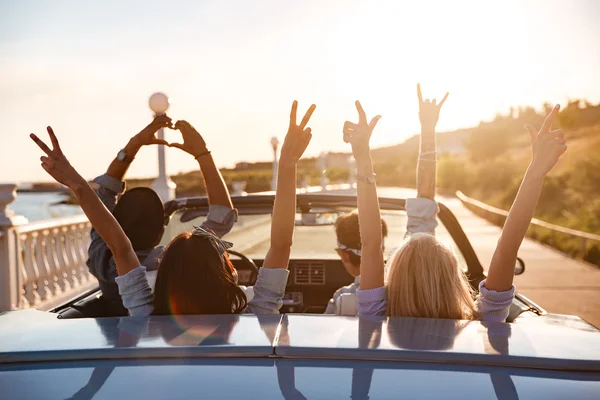 Щасливі друзі в кабріолеті з піднятими руками їздять на заході сонця — стокове фото