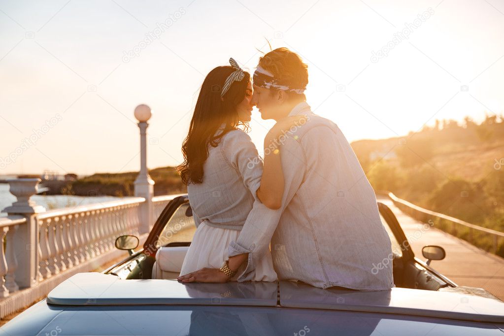 Couple sitting and kissing in car on sunset