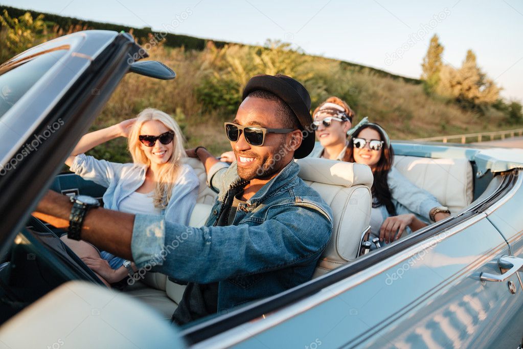 Cheerful young friends driving car and smiling in summer