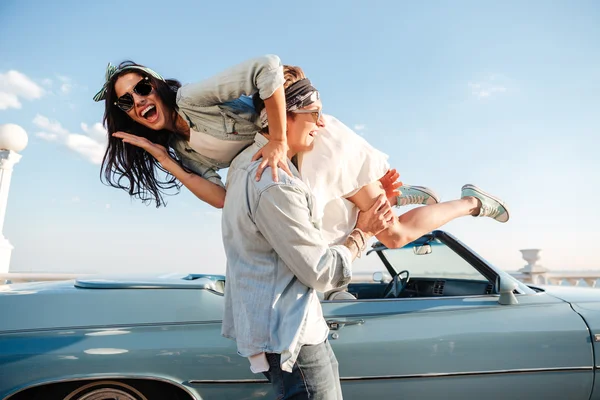 Szczęśliwy młody człowiek, niosąc jego Kobieta, w pobliżu zabytkowych samochodów — Zdjęcie stockowe