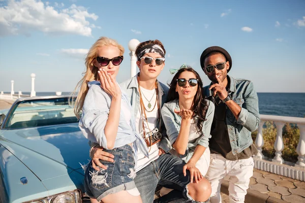 Glückliche junge Leute, die neben einem Oldtimer-Cabriolet stehen und Küsse schicken — Stockfoto