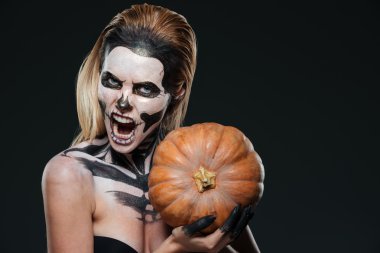 Woman with scared gothic makeup holding pumpkin and shouting
