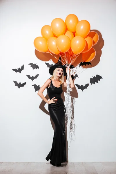 Hermosa joven con disfraz de bruja halloween sosteniendo globos naranjas —  Fotos de Stock