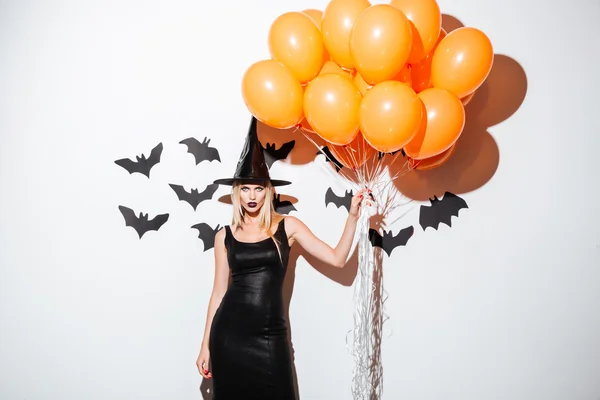 Sexy young woman in witch halloween costume holding orange balloons