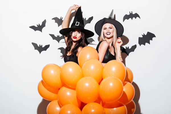 Dos mujeres alegres en trajes de bruja bailando con globos naranjas —  Fotos de Stock