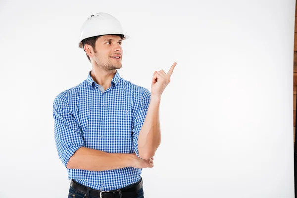 Feliz hombre joven constructor en sombrero duro apuntando lejos —  Fotos de Stock