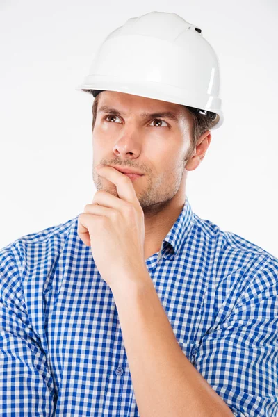 Pensive young man building engineer in helmet standing and thinking — Stock Photo, Image