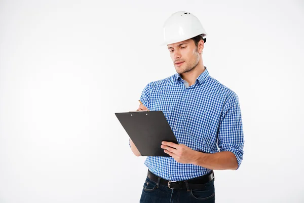 Концентрований молодий чоловік-будівельник у будівництві шолома, що пише на кишені — стокове фото