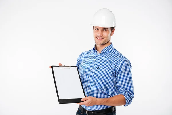 Jovem construtor alegre na construção capacete segurando prancheta em branco — Fotografia de Stock