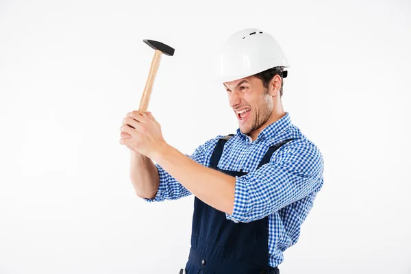 Забавный молодой строитель наносит Хаммер на голову в шлеме — стоковое фото