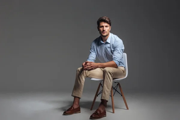 Fundersam brunett mannen i blå skjorta sitter på stolen — Stockfoto