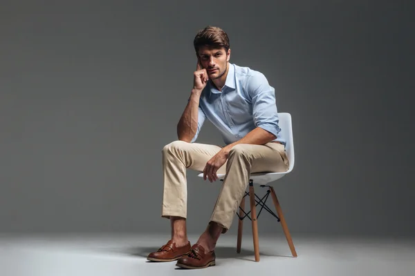 Fundersam brunett mannen i blå skjorta sitter på stolen — Stockfoto