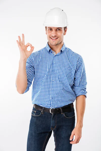 Leende ung man builder i hård hatt visar ok gest — Stockfoto