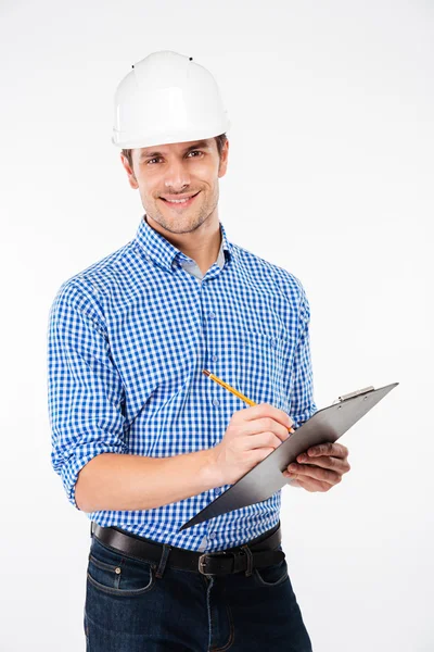 微笑的年轻人建筑师在建筑头盔写作放在剪贴板上 — 图库照片