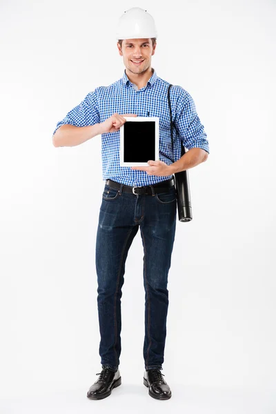 Sonriente hombre arquitecto en el edificio casco celebración de tableta de pantalla en blanco —  Fotos de Stock