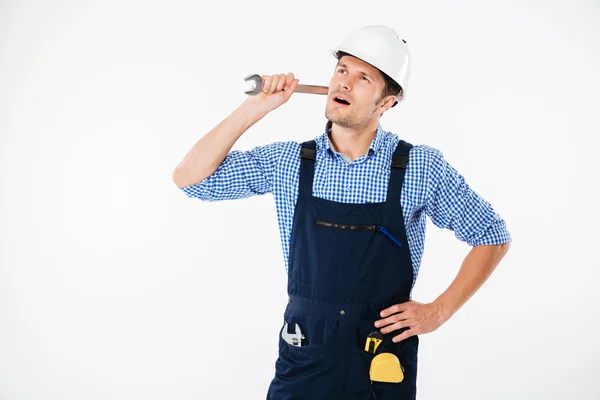 Pensivo bonito jovem construtor pensando e olhando para cima segurando chave inglesa — Fotografia de Stock