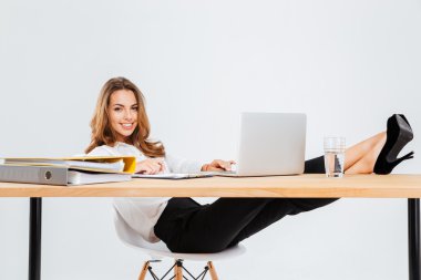 Neşeli iş kadını oturma ve masada bacaklar ile dizüstü bilgisayar kullanarak