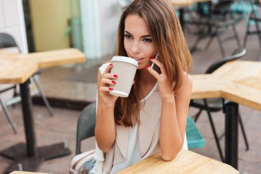 Gülümseyen güzel kadın içme kahve ve cep telefonuyla konuşuyor