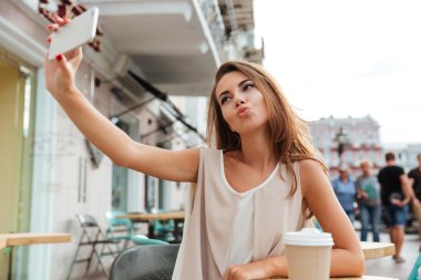 Kafede oturan smartphone ile selfie alarak güzel genç kadın