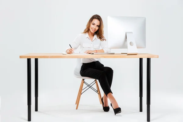 Улыбающаяся счастливая деловая женщина подписывает документы, сидя за столом — стоковое фото