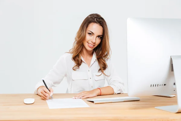 Une jeune femme d'affaires signe des documents alors qu'elle est assise au bureau — Photo